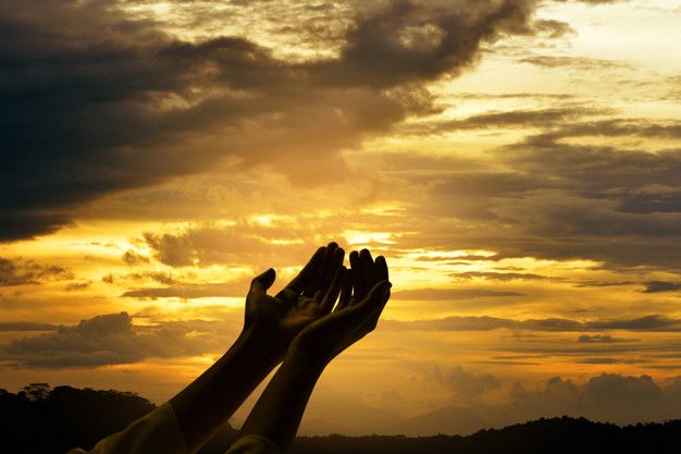 Hands folded in prayer with sunrise background